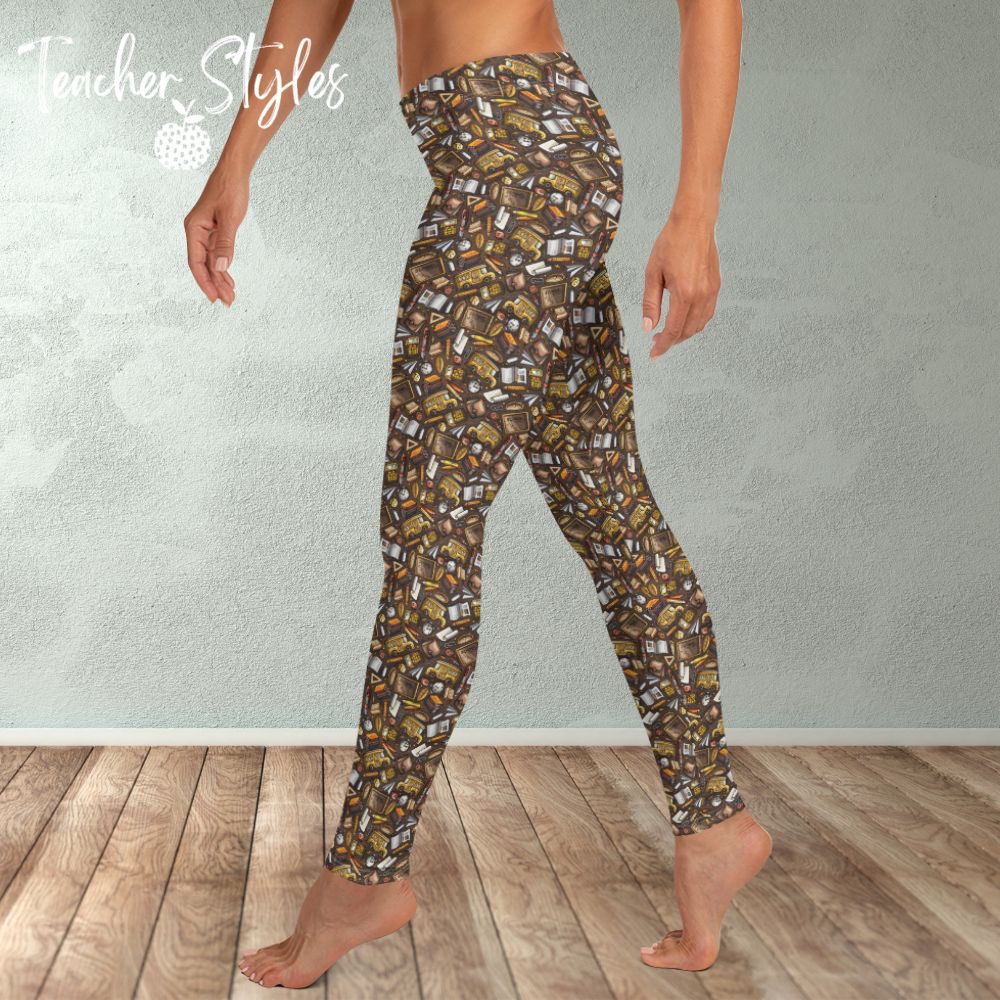 Back to Basics leggings by Teacher Styles. Model is shown from the waist down. Leggings have brown background and pattern of yellow school buses, chalkboards, clocks and more! side view