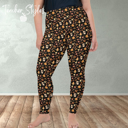 Fall Fun leggings by Teacher Styles. Model is shown from the waist down. Leggings have black background with autumn pattern of pumpkins, pears, apples and flowers. Front view. Plus Size.