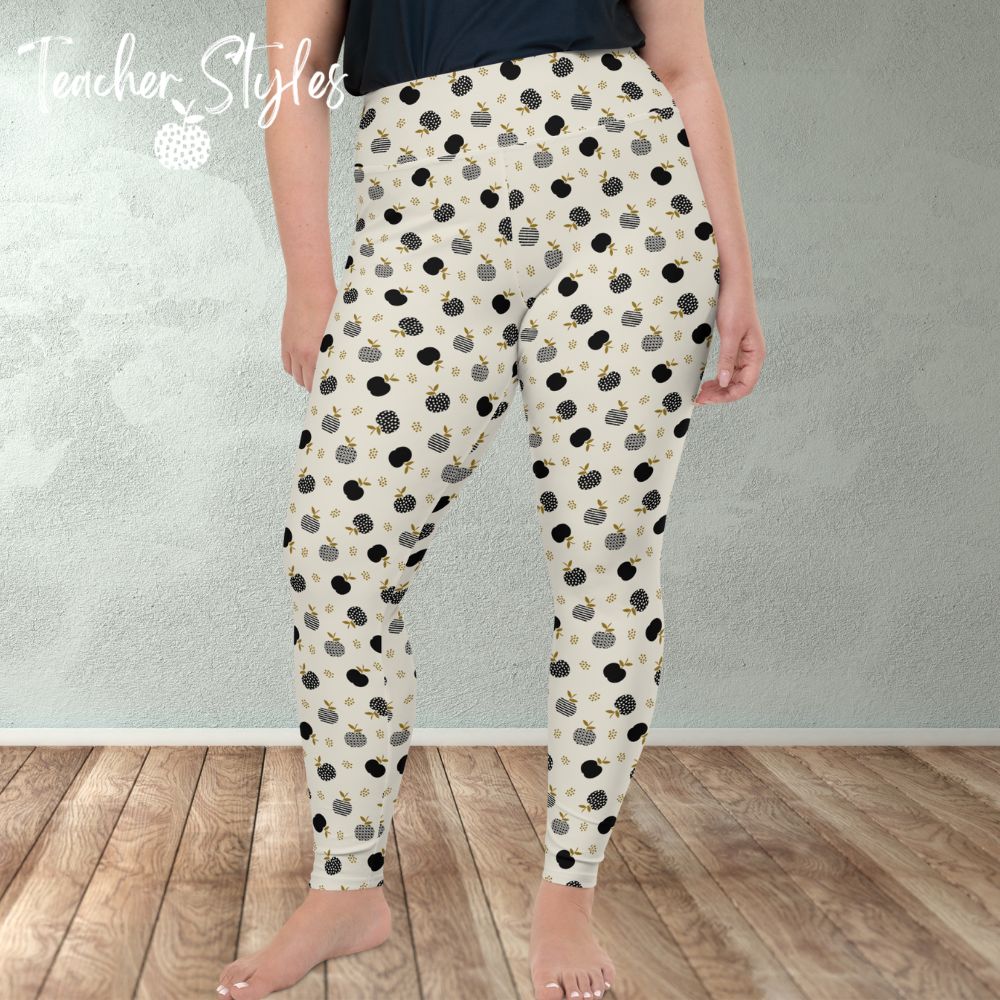 Modern Apple Plus Size Leggings by Teacher Styles. Image of woman from the waist down in room wearing leggings. Front view. Comfortable and stylish light beige/cream leggings featuring a pattern of black apples in solids, stripes and dots.  