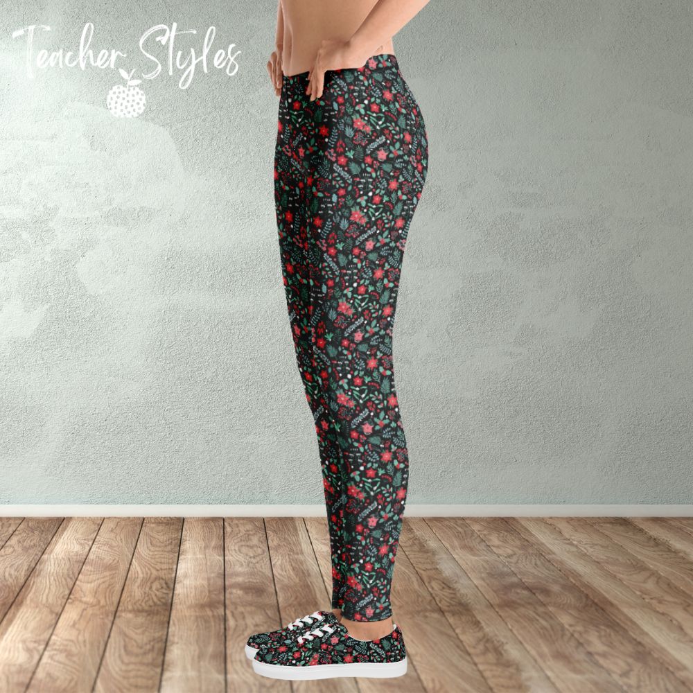 Poinsettia Leggings by Teacher Styles. Model shown from the waist down. Leggings have black background and are covered in a pattern of pointsettia, mistletoe and greenery. Side view. Model is wearing matching shoes