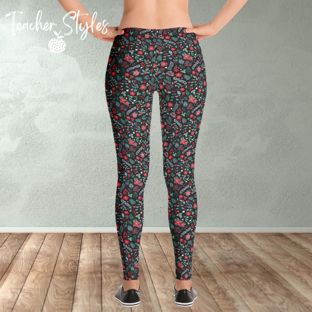 Poinsettia Leggings by Teacher Styles. Model shown from the waist down. Leggings have black background and are covered in a pattern of pointsettia, mistletoe and greenery. Back view