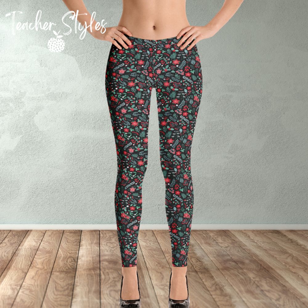 Poinsettia Leggings by Teacher Styles. Model shown from the waist down. Leggings have black background and are covered in a pattern of pointsettia, mistletoe and greenery. Front view