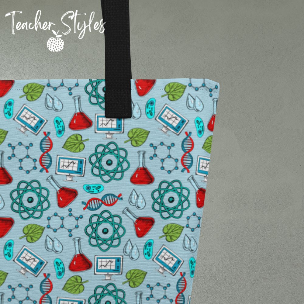 Science Tote Bag by Teacher Styles. Close up detail of large light blue tote with pattern of science graphics - atoms, beakers, DNA and more! Black canvas webbed handles. 