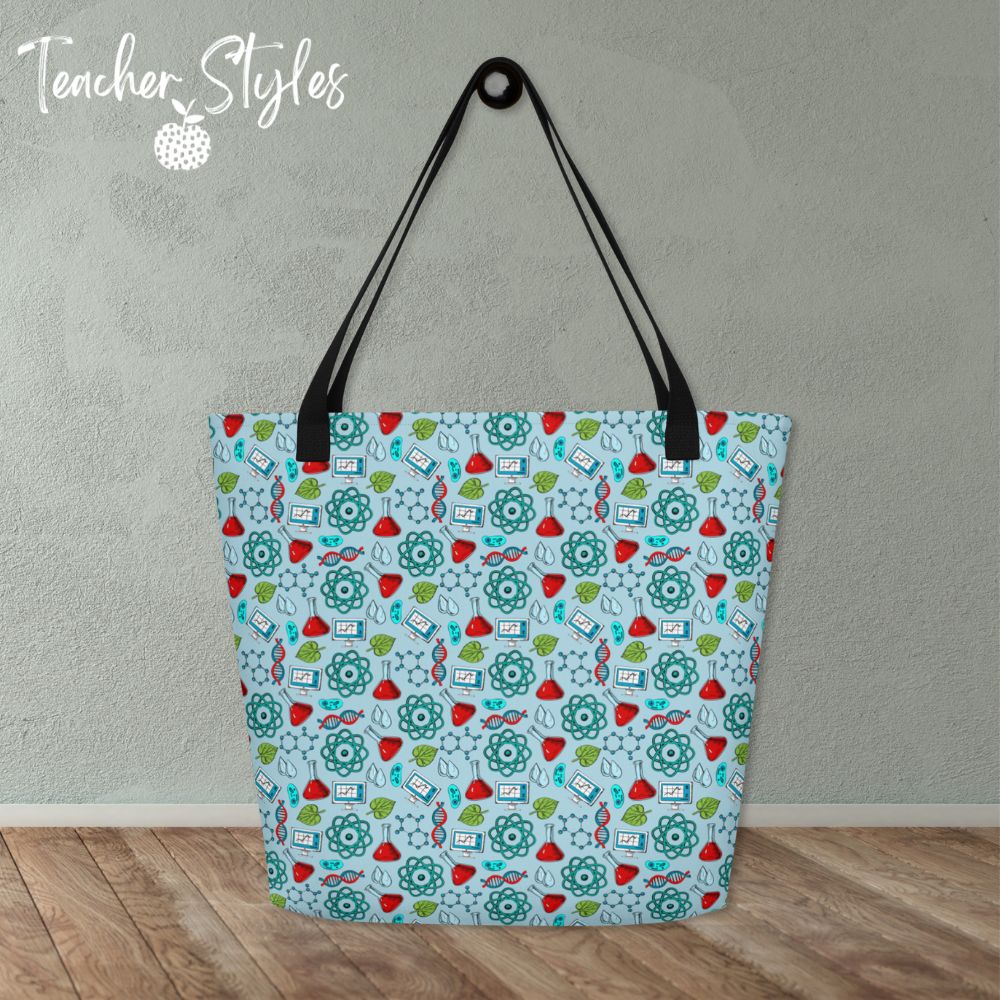 Science Tote Bag by Teacher Styles. Large light blue tote with pattern of science graphics - atoms, beakers, DNA and more! Black canvas webbed handles. Size 16" x 20". on table