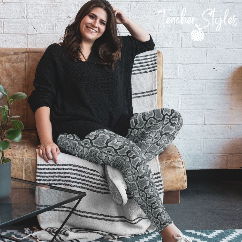 Snake Print leggings by Teacher Styles. Model is shown from the waist down. Leggings are covered in snake skin pattern in various tones of grey. Happy woman is relaxing on the couch